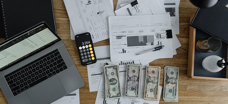 Printed graphs, U. S. dollar bills, the calculator of a mobile phone rest on a desk beside a computer as a reference for payroll software for small businesses -  pexels-tima-miroshnichenko-6693655