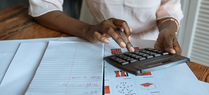 A business woman holds a calculator and makes notes aided with printed charts and
	graphics as she plans to grow with small businesses funding. -  pexels-rodnae-productions-5915230