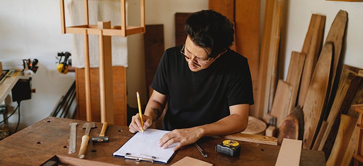 Man takes notes on a table of a wood workshop as a depiction of minority small business -  pexels-ono-kosuki-5973966