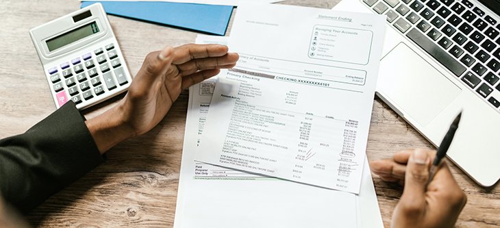 Man works with financial papers, calculator, and a computer on a table as a depiction of Sage accounting software -  pexels-rodnae-productions-7821708