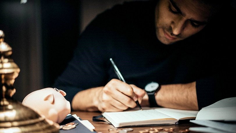 A young male business owner writes balances on a notebook as he calculates the amount needed for a quick cash loan. Photo-credit-Dziana-Hasanbekava-on-Pexels
