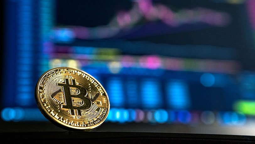 Bitcoin’s logo is displayed on a gold coin against the background of a crypto trading website.