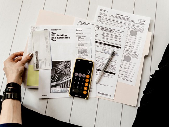 Top shot image of a woman seated on the floor, examining and calculating over tax forms and payments, as they can become part of personal
    finance problems.