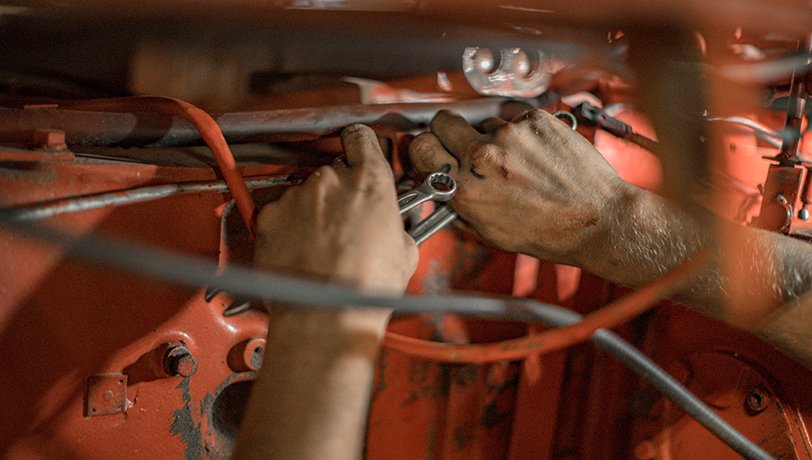 A man does maintenance work under the hood of an old commercial vehicle. nina-mercado-Y_t0n-T4H5M-unsplash
